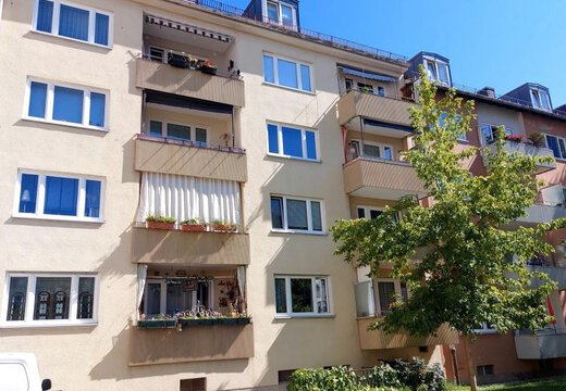 Mehrstöckiges Wohngebäude (Bonner Quartier) in München mit hellgelber Fassade, Balkonen und Gaubenfenstern unter blauem Himmel.