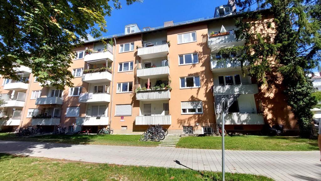 Mehrstöckiges Wohngebäude (Bonner Quartier) in München mit hellgelber Fassade, Balkonen und Gaubenfenstern unter blauem Himmel.