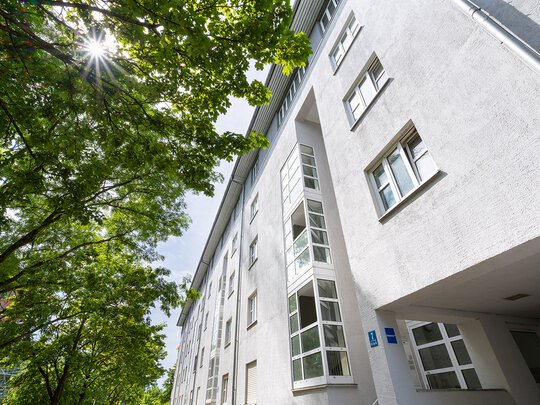 Straßenansicht des Wohngebäudes mit Hauseingang und Laubbäumen an der Straße